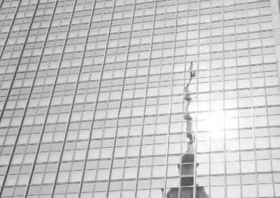 Photo noir et blanc représentant le reflet de la tour de la télévision sur la façade d’un immeuble constitué de carreaux de verre. Artiste, Martes Martes. Lieu, Berlin.