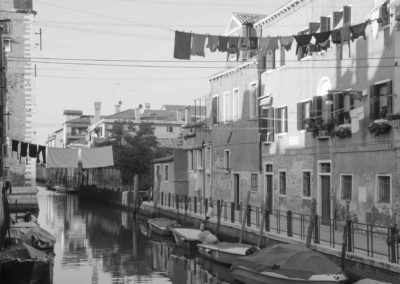Photo noir et blanc représentant une rue de Venise. Le canal est surplombé d’étendage à lessive. Artiste, Martes Martes. Lieu, Venise.