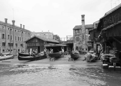 Photo noir et blanc représentant un chantier naval de gondole sur le bord du canal. Artiste, Martes Martes. Lieu, Venise.