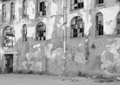 Photo noir et blanc représentant une façade d’usine délabrée. Il n’y a plus de porte et les carreaux des vitres sont cassés. Artiste, Martes Martes. Lieu, Istanbul.