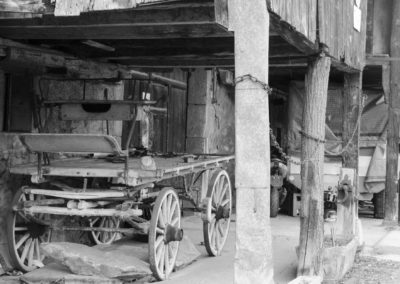 Photo noir et blanc représentant une voiture à cheval abandonnée sous une grange. Artiste, Martes Martes. Lieu, Monthey.